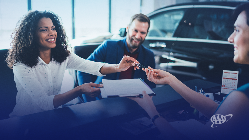 woman taking the keys to her new car from salesperson; man sitting besides her